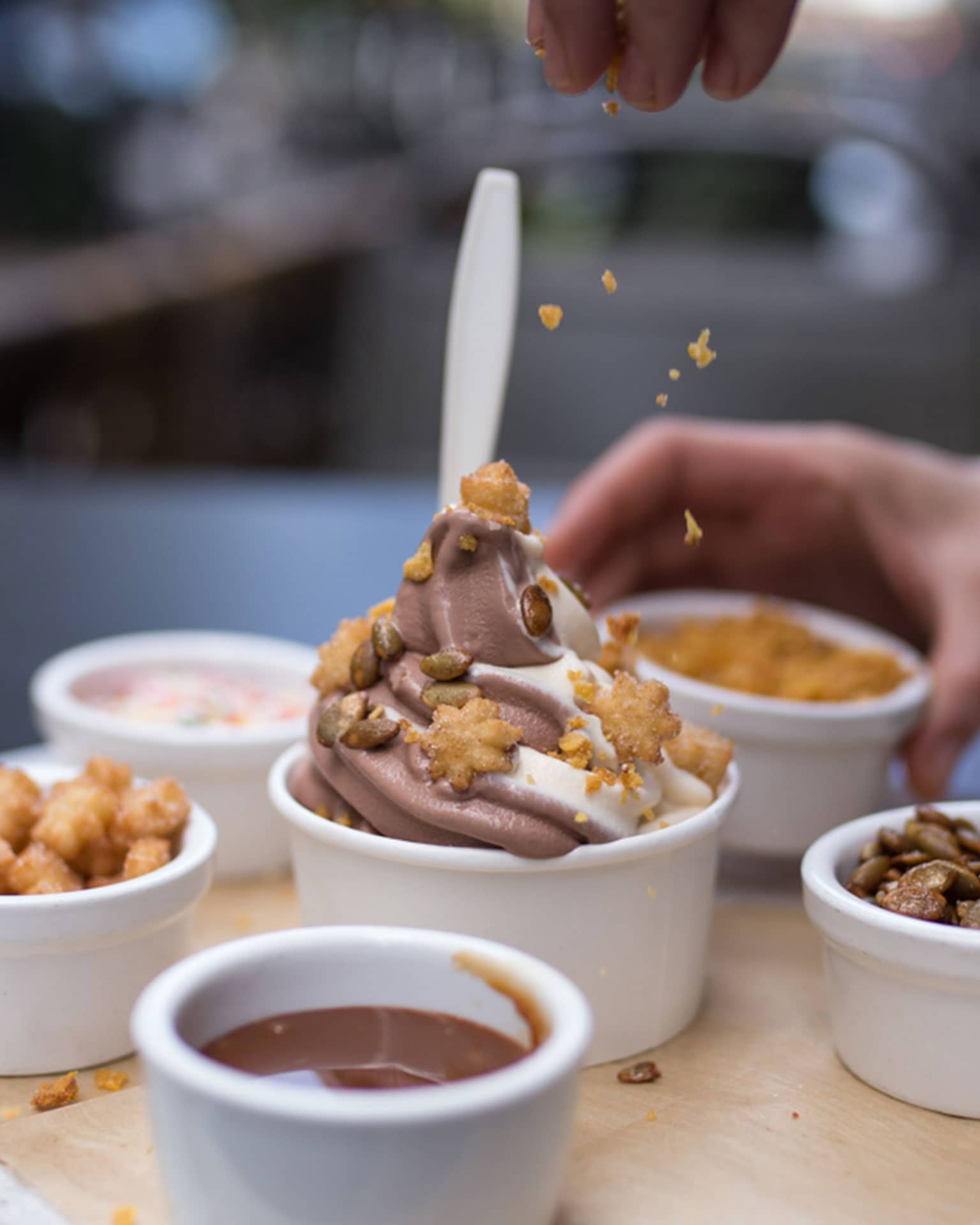 Hand pouring toppings onto bowl of soft serve